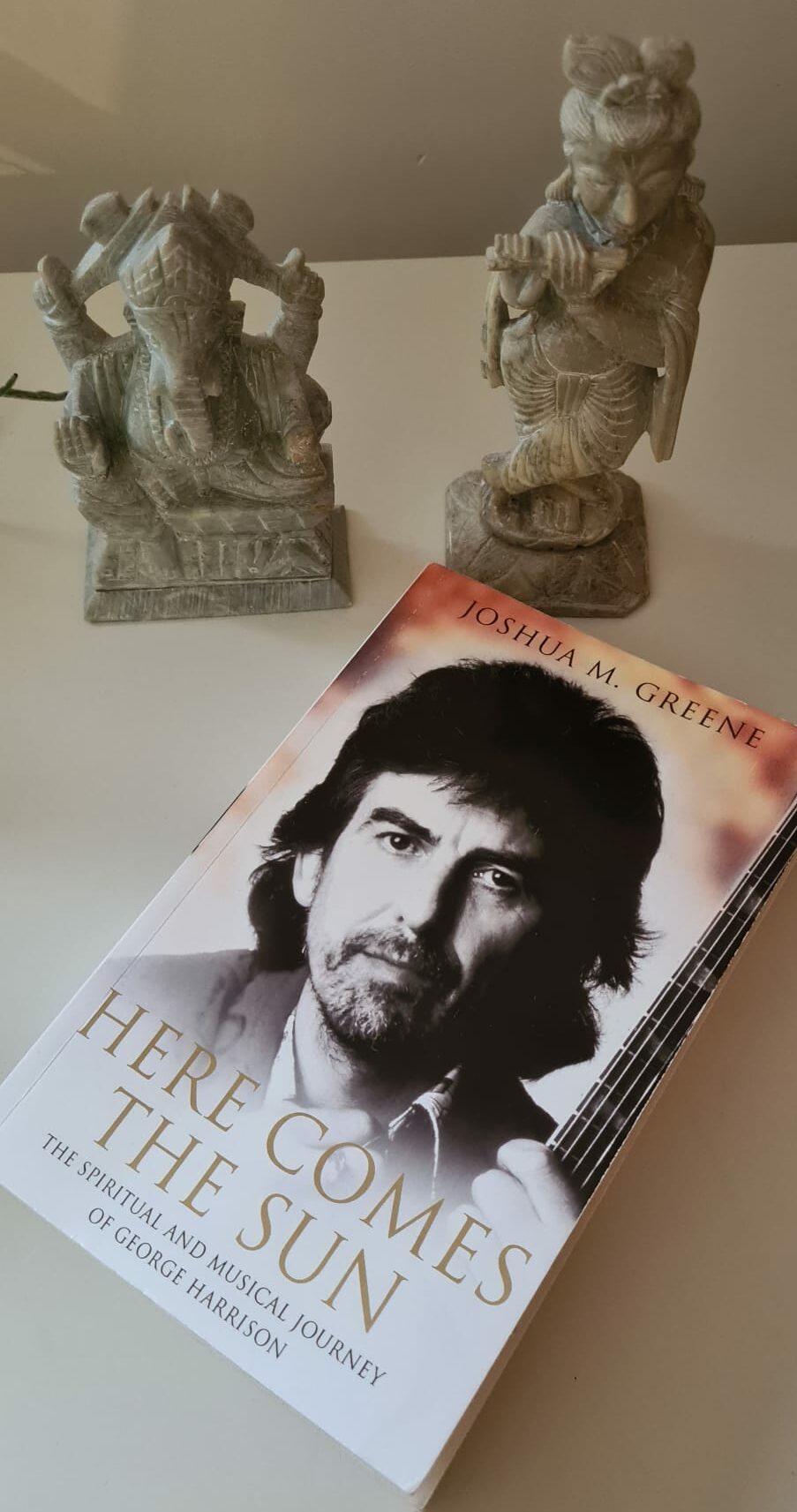 Boek Here Comes The Sun van Joshua M. Greene over George Harrison met daarbij een beeldje van Govinda en Ganesha.