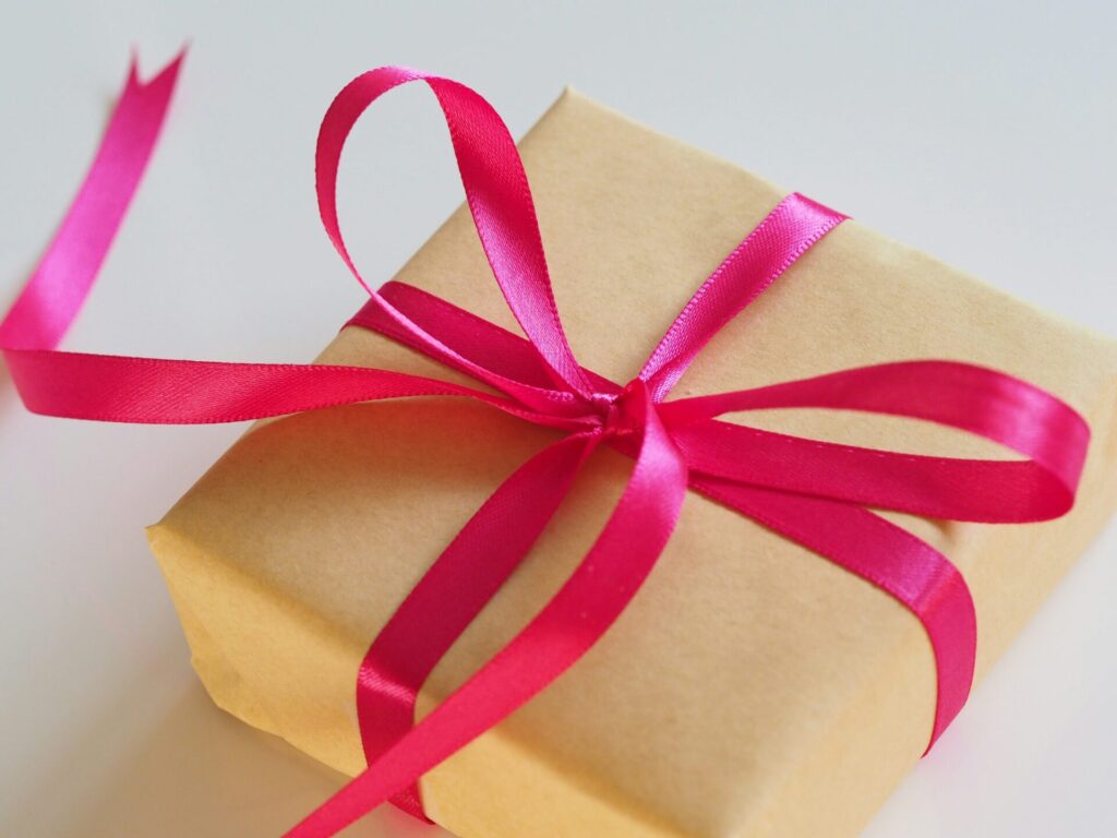 Een pakketje ingepakt met gouden pakpapier en daar omheen een rood lint met een grote strik.