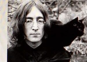 Zwart-wit foto van John Lennon met een zwarte kat op zijn schouder.