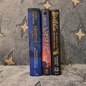 De ruggen van drie boeken staand naast elkaar op een blauw dekentje met witte sterren. De boeken zijn van links naar rechts: Nevermoor - Morrigan Crow en het Wondergenootschap, Witchlings en Starfell - De zoektocht naar afgelopen dinsdag