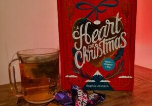Rechts staat het boek a Heart for Christmas (rode kaft) met daar links van een kop thee. Voor het boek liggen chocolaatjes. De achtergrond is een beetje oranjig, de ondergrond is van hout | 3 must-have adventskalenders voor boekenwurmen