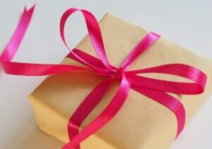 Een pakketje ingepakt met gouden pakpapier en daar omheen een rood lint met een grote strik.