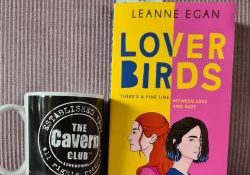 Boek Lover birds van Leanne Egan tegen een roze achtergrond. Links van het boek staat een mok van de Cavern Club.