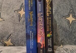 De ruggen van drie boeken staand naast elkaar op een blauw dekentje met witte sterren. De boeken zijn van links naar rechts: Nevermoor - Morrigan Crow en het Wondergenootschap, Witchlings en Starfell - De zoektocht naar afgelopen dinsdag